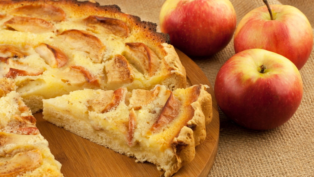 Torta de maça fatiada com um pedaço em destaque e a fruta ao lado