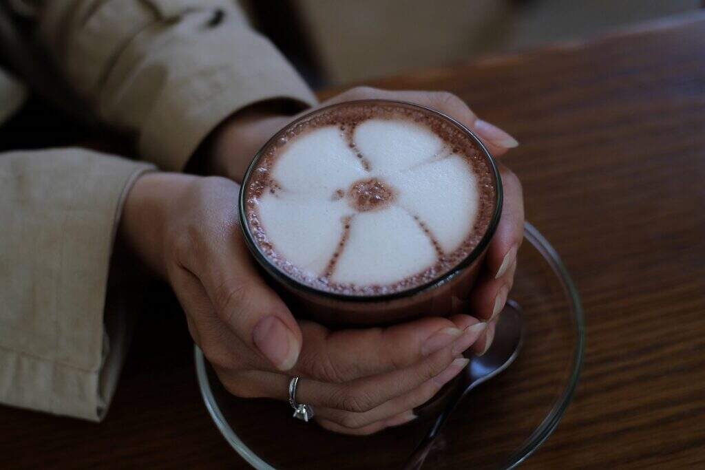 Mulher segurando com as duas mãos uma café gourmet com latteart