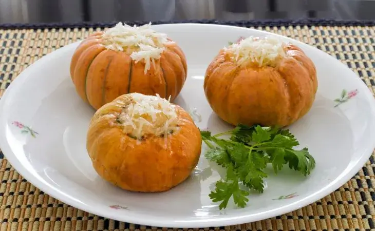 Mini abóboras laranjas recheadas com carne e queijo ralado por cima em um prato branco com coentro para servir de enfeite - receitas divertidas de halloween